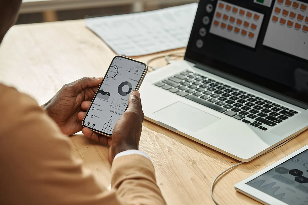 Person using smartphone to analyze business data visualizations on mobile screen next to laptop
