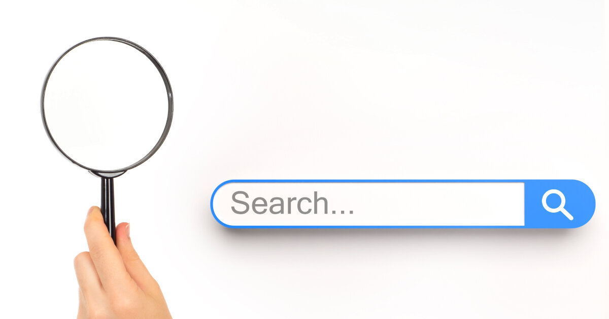 A hand holding a magnifying glass next to a search bar