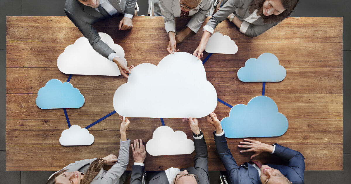 Business people around a table holding cloud icons 
